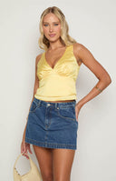 Yellow v-neckline satin cropped top with open tie back and styled with a denim mini skirt 